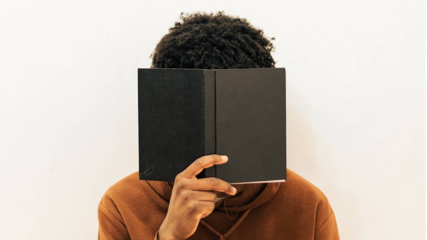 Student hiding their face behind a book. Photo by Marc Yusufu.