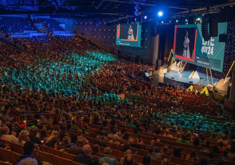 A photo of a conference arena stage and the seated audience taken from high up in the back of the arena. On the stage and big screen monitors are the logo for ISTELive 24.